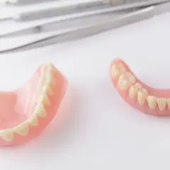 Protesi dentarie, superiori e inferiori, su sfondo bianco, con strumenti dentistici sfocati sullo sfondo. Soluzione per denti mobili.