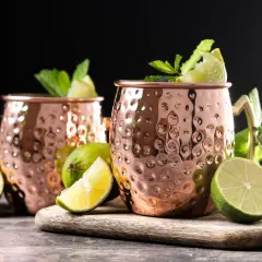 Due tazze di rame martellato per un Moscow Mule, guarnite con menta fresca e spicchi di lime.