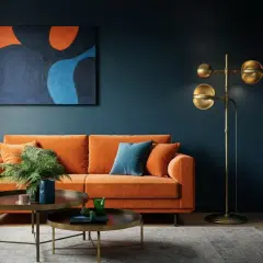 Ein orangefarbenes Sofa und ein abstraktes Gemälde schaffen ein warmes Wohnzimmer. Ein Messing-Stehleuchte sorgt für gemütliches Licht.