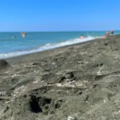 Ciemny piasek na plaży w Ureki, Gruzja. W tle widać turkusowe morze i kąpiących się ludzi.