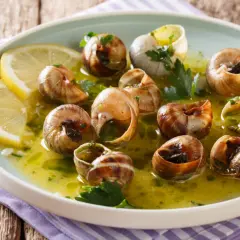 Escargot to danie z gotowanych ślimaków w sosie czosnkowo-ziołowym, podane z plasterkami cytryny.