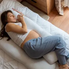 Femme enceinte dormant sur le côté, soutenue par un coussin, cherchant le confort pour éviter la remontée acide grossesse nuit.