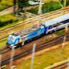 Pędzący pociąg "Adriatic Express" na trasie z Warszawy do Łodzi, z rozmytym tłem zieleni i torów.