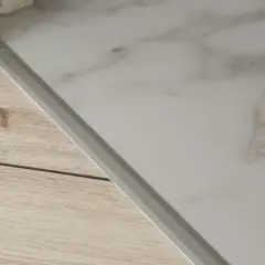 Un battiscopa in laminato effetto metallo separa un pavimento in finto marmo da uno in finto legno.
