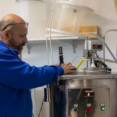 Mann in blauer Jacke überwacht Gärprozess. Hier wird die Frage "was ist Essig?" beantwortet, indem die Herstellung gezeigt wird.
