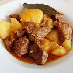 Sabroso morcillo de ternera guisado con patatas y una hoja de laurel, servido en un plato blanco.