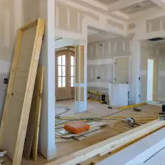 Wnętrze w trakcie przebudowy. Leżące drzwi, materiały budowlane i narzędzia na podłodze.