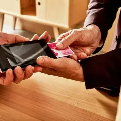 Dwie dłonie zbliżają kartę do terminala płatniczego. To prosty sposób, jak doładować telefon na kartę.