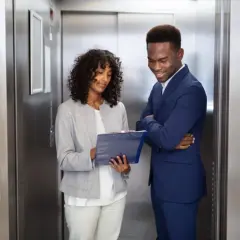 Zwei Geschäftsleute im Aufzug, die Notizen besprechen. Ein kurzer elevator pitch, bevor die Türen sich öffnen.