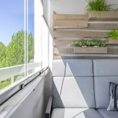 Nowoczesny balkon z szarą sofą i wiszącymi donicami z ziołami i sałatą. Idealne balkon inspiracje dla miłośników zieleni.
