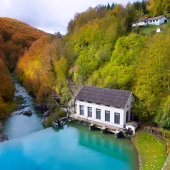 Embalse de agua turquesa junto a una central eléctrica, rodeado de bosques otoñales. Ideal para rutas selva de Irati.
