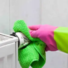 Mano con guanto rosa e verde pulisce il termostato del termosifone con un panno verde. Guida su come pulire i termosifoni.