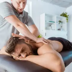 Fizjoterapeuta wykonuje masaż sportowy na plecach mężczyzny leżącego na kozetce.