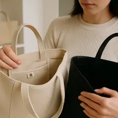 En person håller upp två fina märkesväskor, en i beige och en i svart.