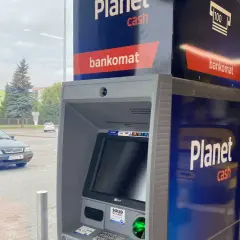 Bankomat Santander Planet Cash przy parkingu. Obok stoi czarny samochód.