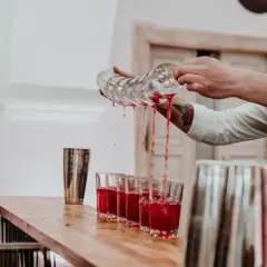 Barman nalewa czerwony napój do kieliszków na weselu, obok podekscytowana panna młoda.