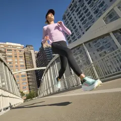 Kobieta w sportowym stroju biegnie po moście w mieście, w tle budynki.