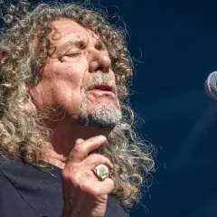 Wokalista Led Zeppelin, Robert Plant, śpiewa do mikrofonu, z charakterystyczną burzą kręconych włosów.