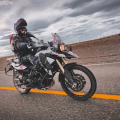 Motocyklista w kasku i kurtce pędzi na motocyklu BMW F 800 po pustej drodze pod burzowym niebem.