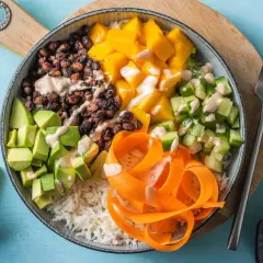En färgglad poke bowl med ris, svarta bönor, mango, gurka, avokado och morotsstrimlor, toppad med en krämig dressing.