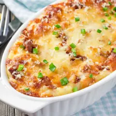 Zapiekanka makaronowa z kurczakiem, posypana szczypiorkiem i parmezanem, w białej naczyniu żaroodpornym.