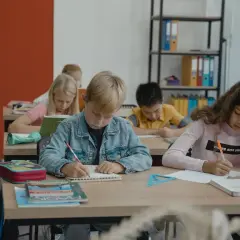 Dzieci piszą w zeszytach, ale jedno z nich, z fobią szkolną, czuje się zagubione.