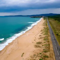 Bułgaria jakie morze? Piękna, turkusowa woda obmywa piaszczystą plażę, a w oddali widać zabudowania i zielone wzgórza. Droga wzdłuż wybrzeża zaprasza do podróży.