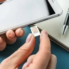 Dłoń wyjmuje kartę SIM z telefonu. Na biurku leży notatnik i długopis. To ważny numer na kartę.