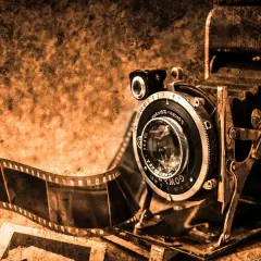 Stary aparat składany i taśma filmowa, symbolizujące historię aparatu fotograficznego.