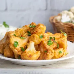 Coliflor rebozada al horno, dorada y crujiente, adornada con perejil fresco. Un plato delicioso y saludable.