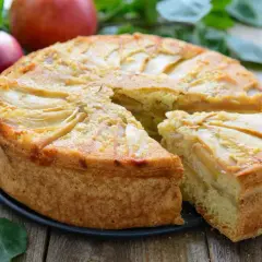 Deliziosa torta di mele vegana con fette di mela disposte a raggiera sulla superficie dorata. Una fetta è già stata servita.