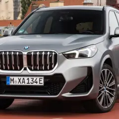 Srebrny x1 bmw z charakterystyczną atrapą chłodnicy i nowoczesnymi światłami, zaparkowany na tle miejskiej panoramy.
