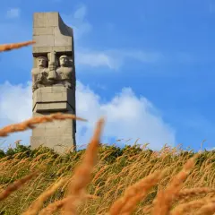 Pomnik Obrońców Wybrzeża na Westerplatte podczas zwiedzania. W oddali widać dwie kamienne postacie żołnierzy.