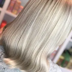 En person med vackert, ljust blondt hår som har fått en ny depend hårfärg. Håret är rakt och glansigt, med en mjuk övergång från mörkare till ljusare toner.