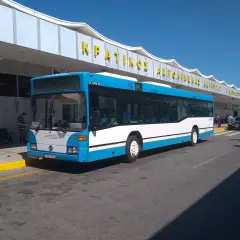 Niebiesko-biały autobus na Korfu, symbol komunikacji miejskiej, czeka na pasażerów przed budynkiem lotniska.