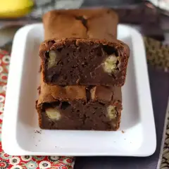 Dos porciones de bizcocho de plátano y chocolate apiladas, con trozos de plátano visibles en su interior.