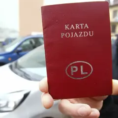 Czerwona karta pojazdu z napisem "KARTA POJAZDU" i symbolem "PL" w owalu, trzymana przed białym samochodem.