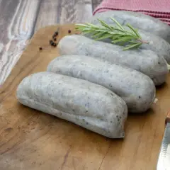 Saucisses grises sur planche en bois, avec romarin et poivre. La différence entre andouille et andouillette est subtile, mais la texture ici suggère une andouillette.
