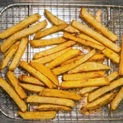 Nyligen friterade pommes frites ligger på ett galler i en metallbricka. De är gyllene och ser krispiga ut.