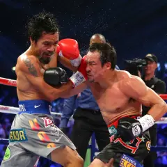 Manny Pacquiao lands a punch on Juan Manuel Marquez during their intense boxing match. Sweat flies as the crowd roars.