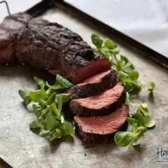 Perfekt grillad oxfilé, saftig och röd i mitten, serverad med färska gröna blad på en rustik plåt. En riktig höjdare för grillmästaren!