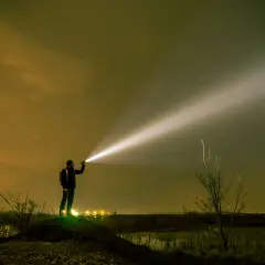 Mężczyzna z plecakiem oświetla nocne niebo potężnym snopem światła z latarki o dużym zasięgu.