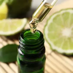 Une goutte d'huile essentielle de bergamote tombe d'une pipette dans un flacon vert. Un remède de grand-mère pour lutter contre la fatigue, entouré de fruits coupés.