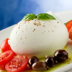 Bufala mozzarella z pomidorkami koktajlowymi i oliwkami na białym talerzu, skropiona oliwą.