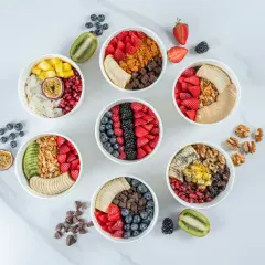 Sju skålar med färgglada frukter, granola och nötter. Perfekta för nyttiga snacks recept som ger energi.