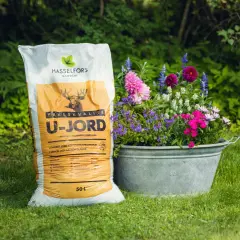En säck Hasselfors U-jord, perfekt för sommarblommor, bredvid en zinkbalja fylld med blommor. Jorden är kalkrik och ger näring.
