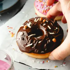 Leckeres Schoko-Donut-Rezept für den Backofen. Ein Donut mit Schokoglasur und Streuseln wird von einer Hand gehalten.