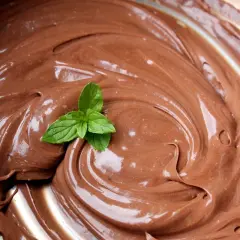 Una fogliolina di menta fresca adorna una spirale di lucida ganache al cioccolato, invitando a un assaggio goloso.