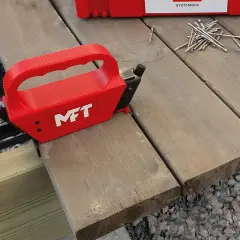 Röd MFT-apparat för att skruva trall dolt. En hög med skruv ligger redo.