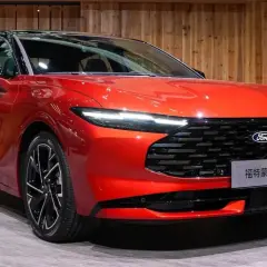Nowy, lśniący, czerwony Ford Mondeo MK5 z czarnym dachem i felgami prezentuje się elegancko na tle drewnianej ściany.